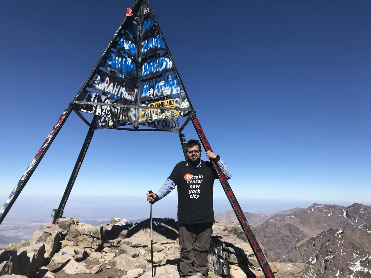 Hamdan standing beneath the metal summit marker on Mount Toubkal