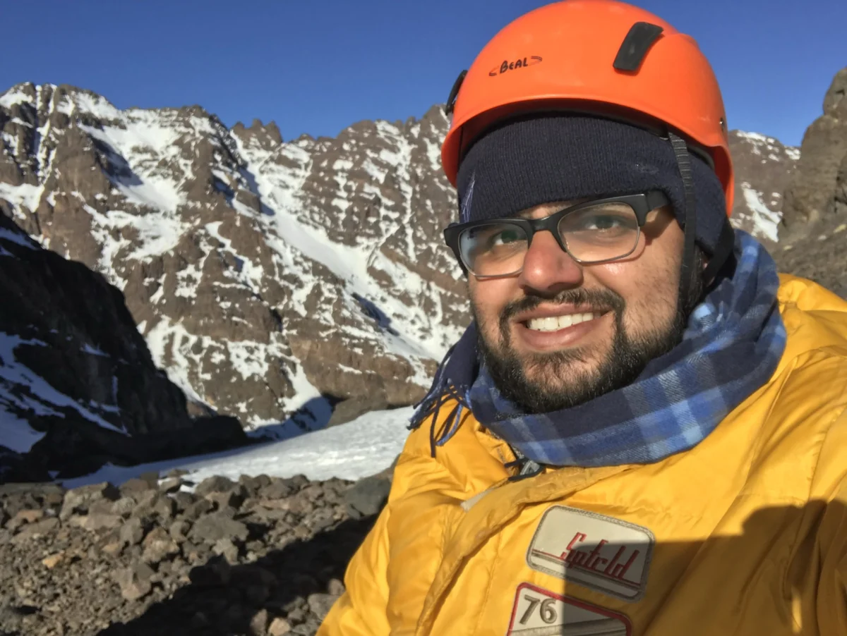 Hamdan in an orange helmet and yellow jacket on snowy Mount Toubkal