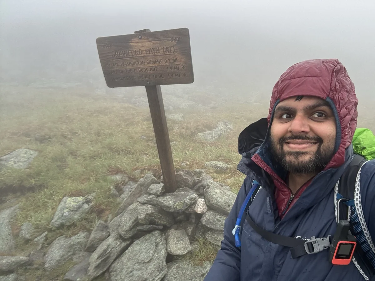 Hamdan wearing a red hood beside a trail sign in dense cloud