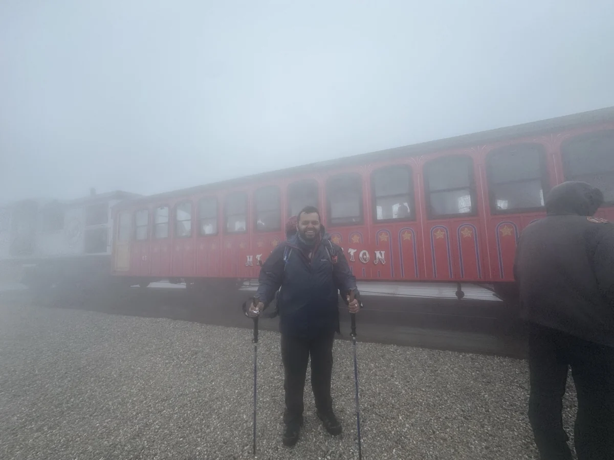 Hamdan standing beside a red Mount Washington Cog Railway carriage in fog
